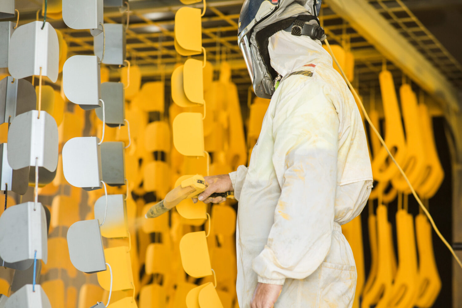 Person in protective clothing spray painting metal parts in yellow